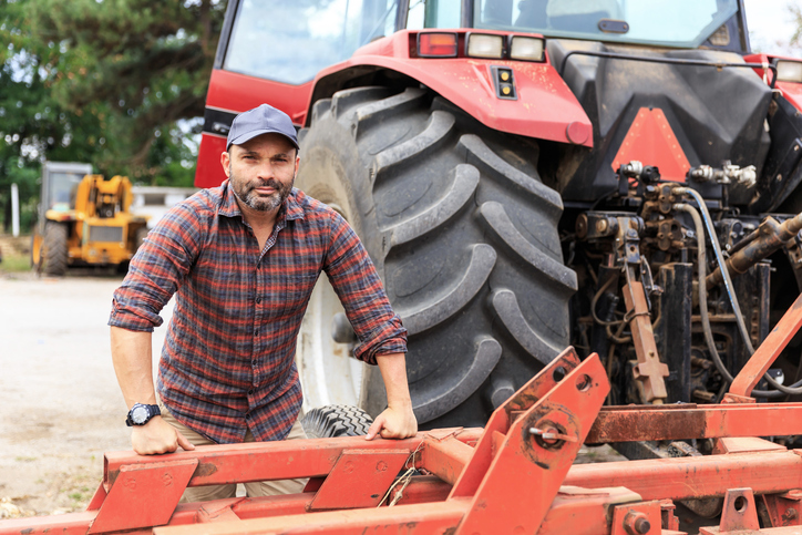 farmer standing in front of his tractor equipment. tractor alternators are needed to power their livelihood. 